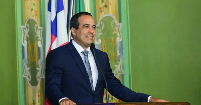 prefeito Bruno Reis em um púlpito durante a coletiva de imprensa, gesticulando de forma assertiva, com o brasão da Prefeitura de Salvador ao fundo. A imagem deve transmitir liderança e decisão. Foco no prefeito, com os jornalistas levemente desfocados em primeiro plano ou ao fundo.
